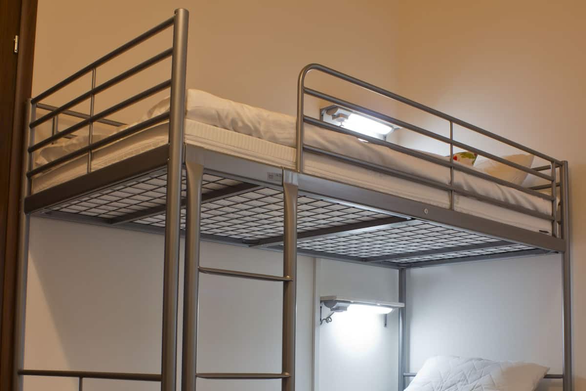 Una litera con estructura metálica, un colchón blanco y una pequeña estantería con luz.