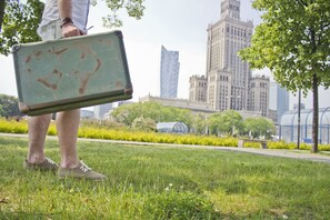 A person holding a suitcase in a park with buildings in the background.