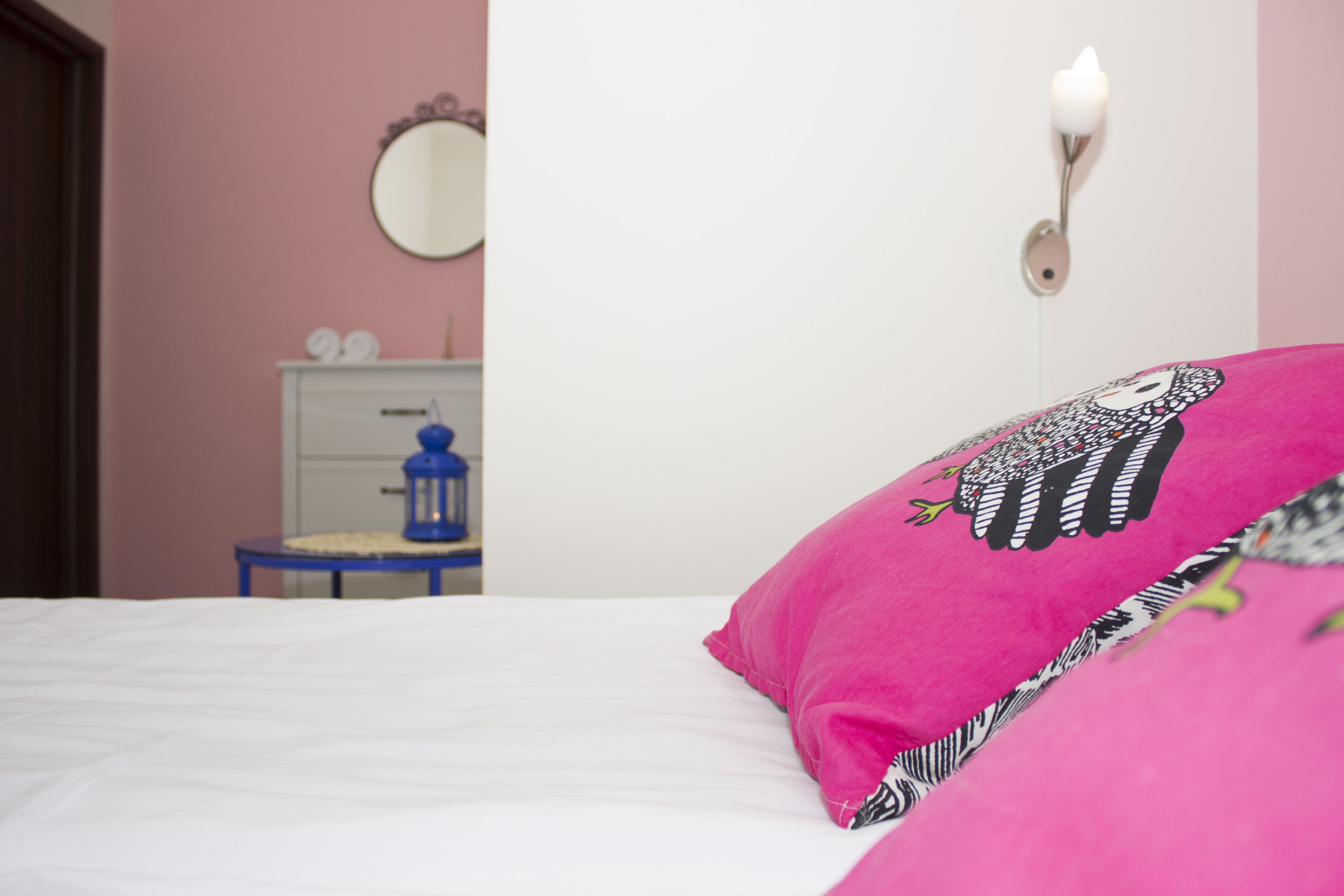 Une chambre à coucher comprenant un lit, une commode, un miroir et un luminaire fixé au mur.