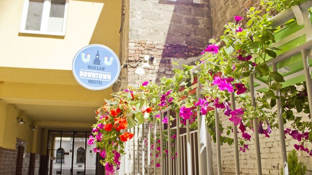 Un letrero de albergue, una pared de ladrillo y una barandilla de metal con flores.