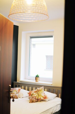 A bedroom with a bed, a window with a view, a plant on the windowsill, and a hanging light fixture.