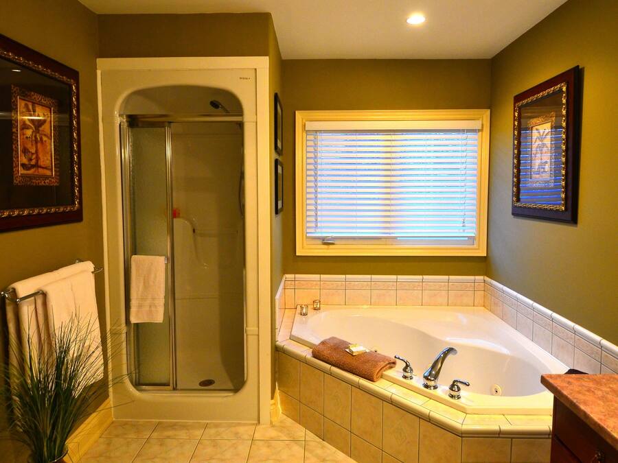 A bathroom with a glass-enclosed shower, a freestanding bathtub, and a window with blinds.