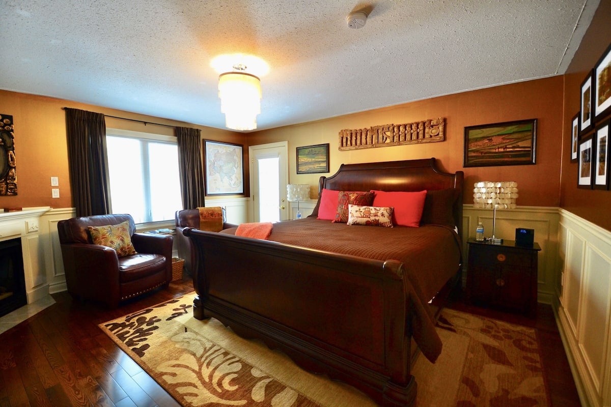 A bedroom with a large bed, a chair, a nightstand, and a fireplace.