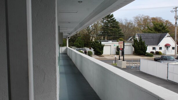 A covered outdoor area with a concrete barrier, a view of a building with a garage, and a signboard. - Budget Inn Motel Suites (Somers Point)