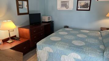 Habitación de hotel con cama, escritorio con lámpara, televisión, microondas y cómoda.