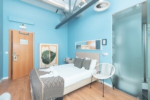 A modern hotel room with a large bed, a bedside table, a chair, and a glass partition wall. - Lisbon Destination Hostel (Lisbon)