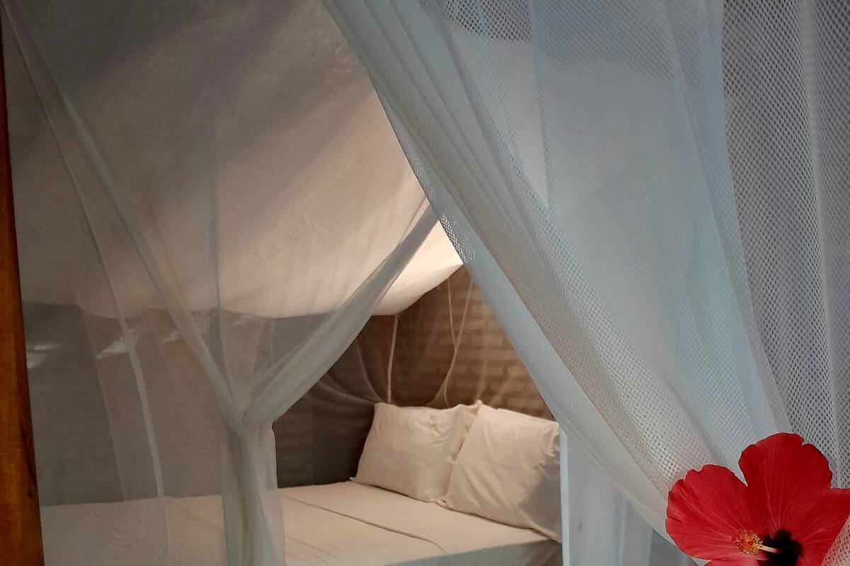 A bed with a canopy and a red hibiscus flower decoration.