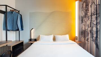 Ein modernes Hotelzimmer mit einem ordentlich bezogenen Bett, einem Nachttisch mit Lampe, einem Kleiderhaken und einer Wand mit Wellenmuster.