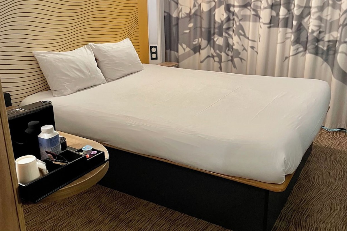 Een hotelkamer met een bed, nachtkastje en een muur met een golvend patroon.