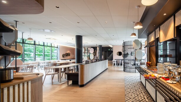 A modern restaurant with a long counter, seating area, and large windows.