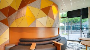 A modern lounge area with a curved seating arrangement, a wooden side table, and a large window offering a view of the outdoors.