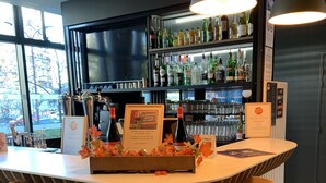 A bar area with a wooden bar counter, two bar stools, and a shelf with various bottles and glasses.