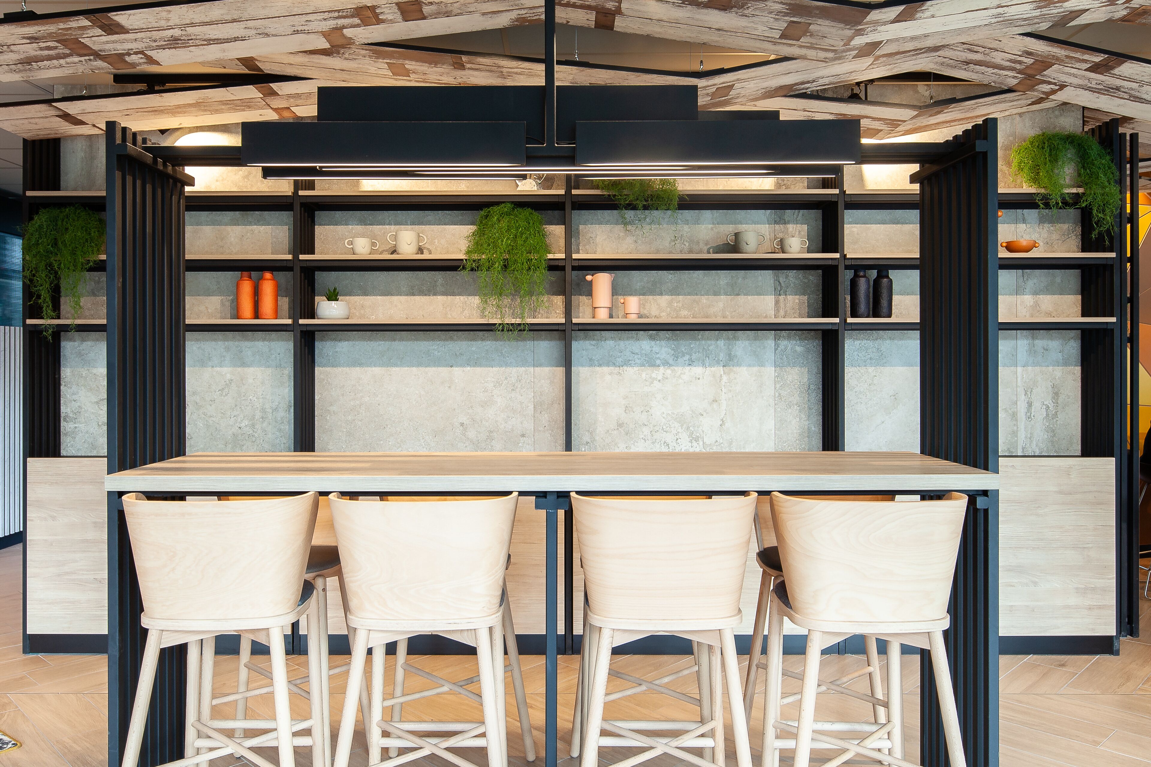 A modern kitchen with a wooden table and three chairs, shelves with kitchenware, and hanging plants.