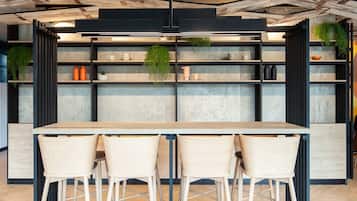 A modern kitchen with a wooden table and three chairs, shelves with kitchenware, and hanging plants.