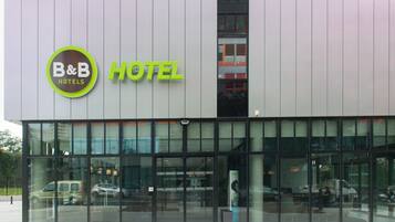Een modern hotel met een glazen gevel, een opvallend B&B Hotels logo en een duidelijke ingang.