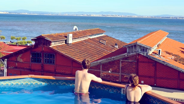 A swimming pool with a view of the ocean and distant mountains. - Sunset Destination Hostel (Lisbon)