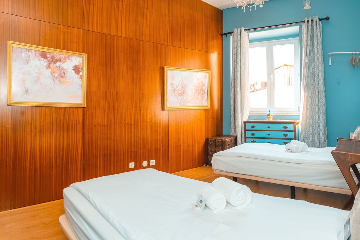 A hotel room with wooden paneling, two beds, a dresser, a mirror, and artwork on the walls.
