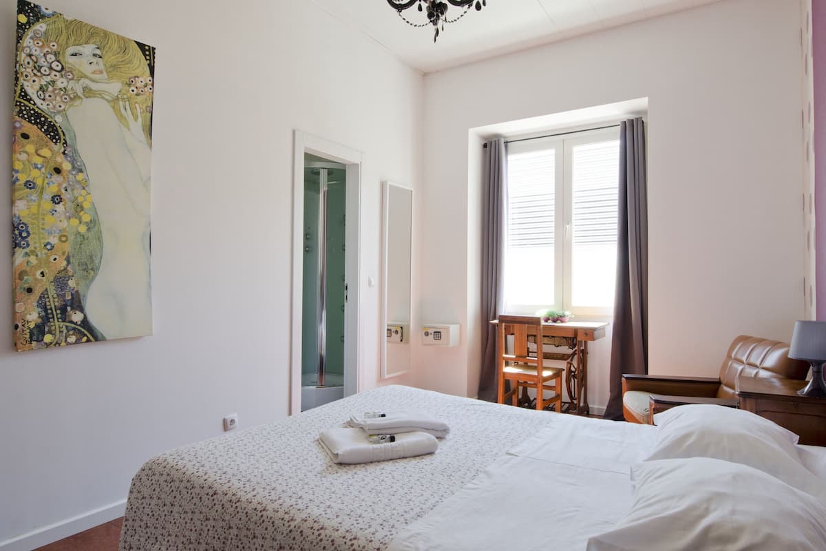 A hotel room with a bed, a desk, a chair, a leather sofa, and a large painting on the wall.