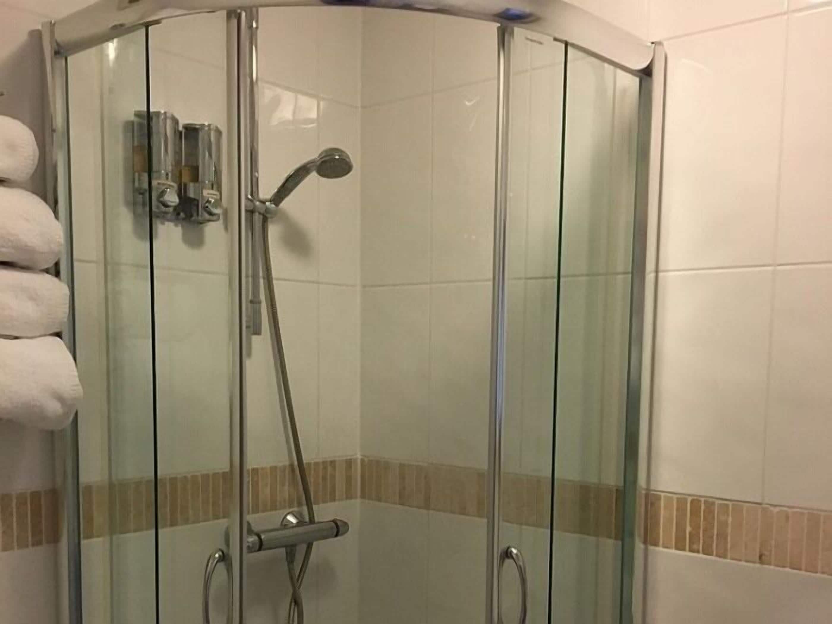 A glass-enclosed shower stall with a handheld showerhead and a wall-mounted control panel.