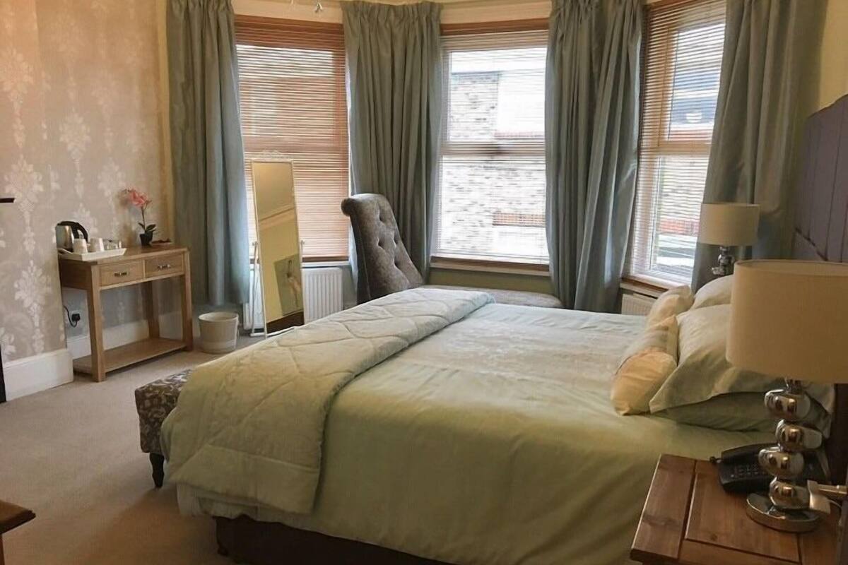 A bedroom with a large bed, a desk, a chair, and a lamp.