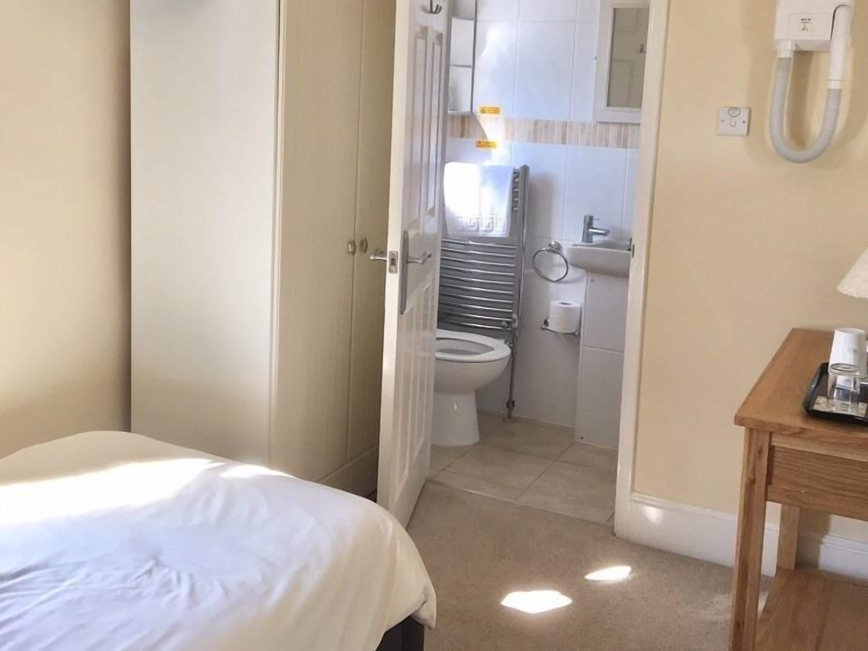 A hotel room with a bed, a wooden side table, a toilet, and a sink.