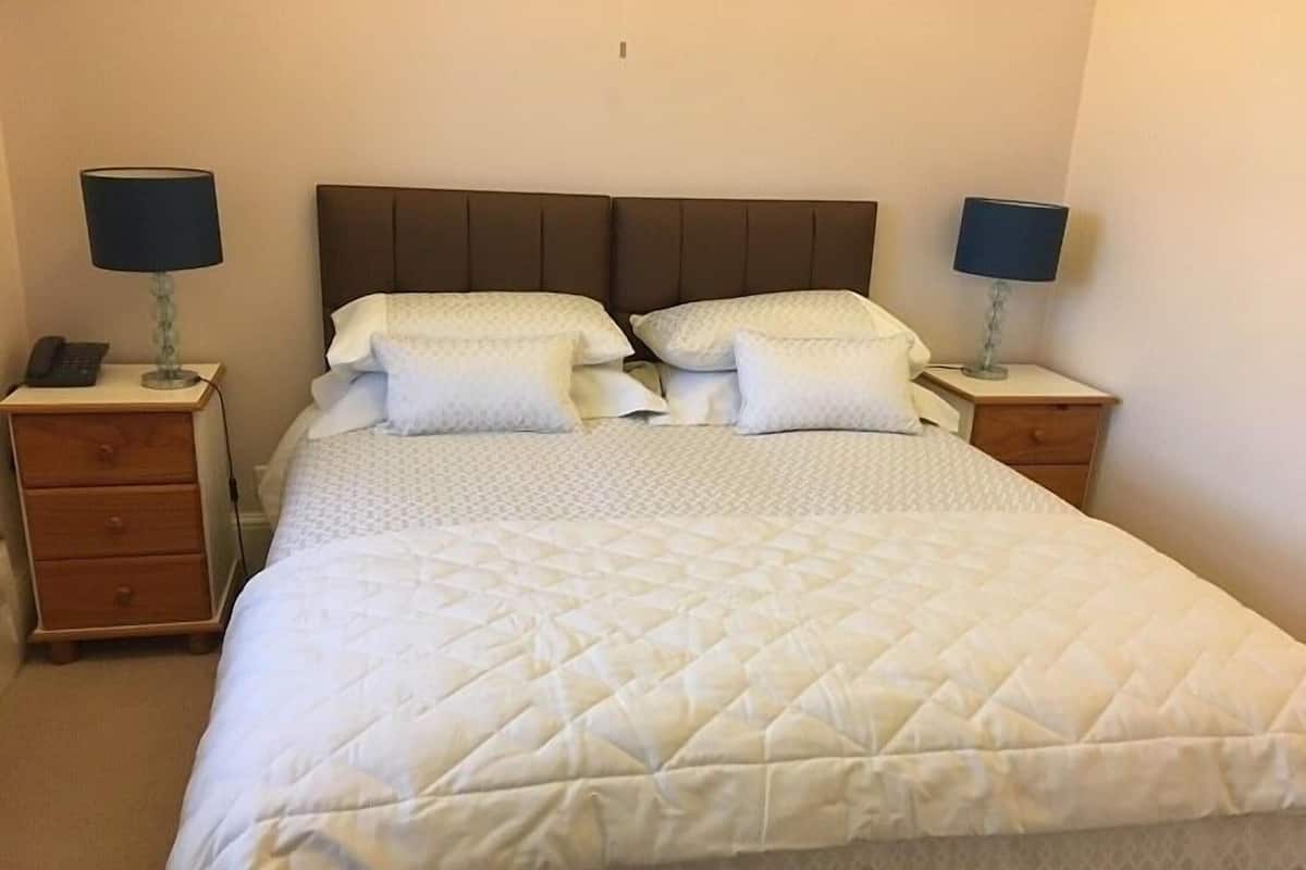 A neatly made bed with a quilted white duvet, two bedside tables with lamps, and a wooden nightstand with a phone.