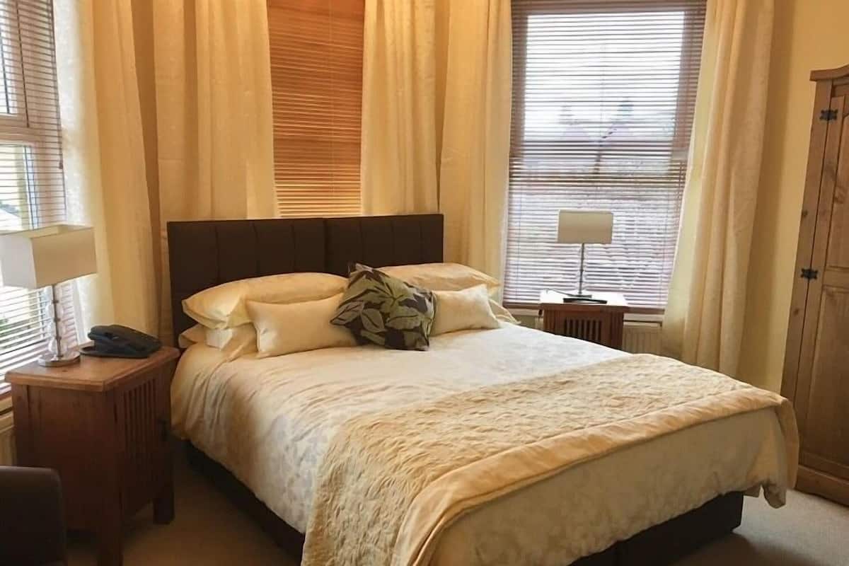 A neatly made bed with a headboard, a bedside table with a lamp, and a chair.