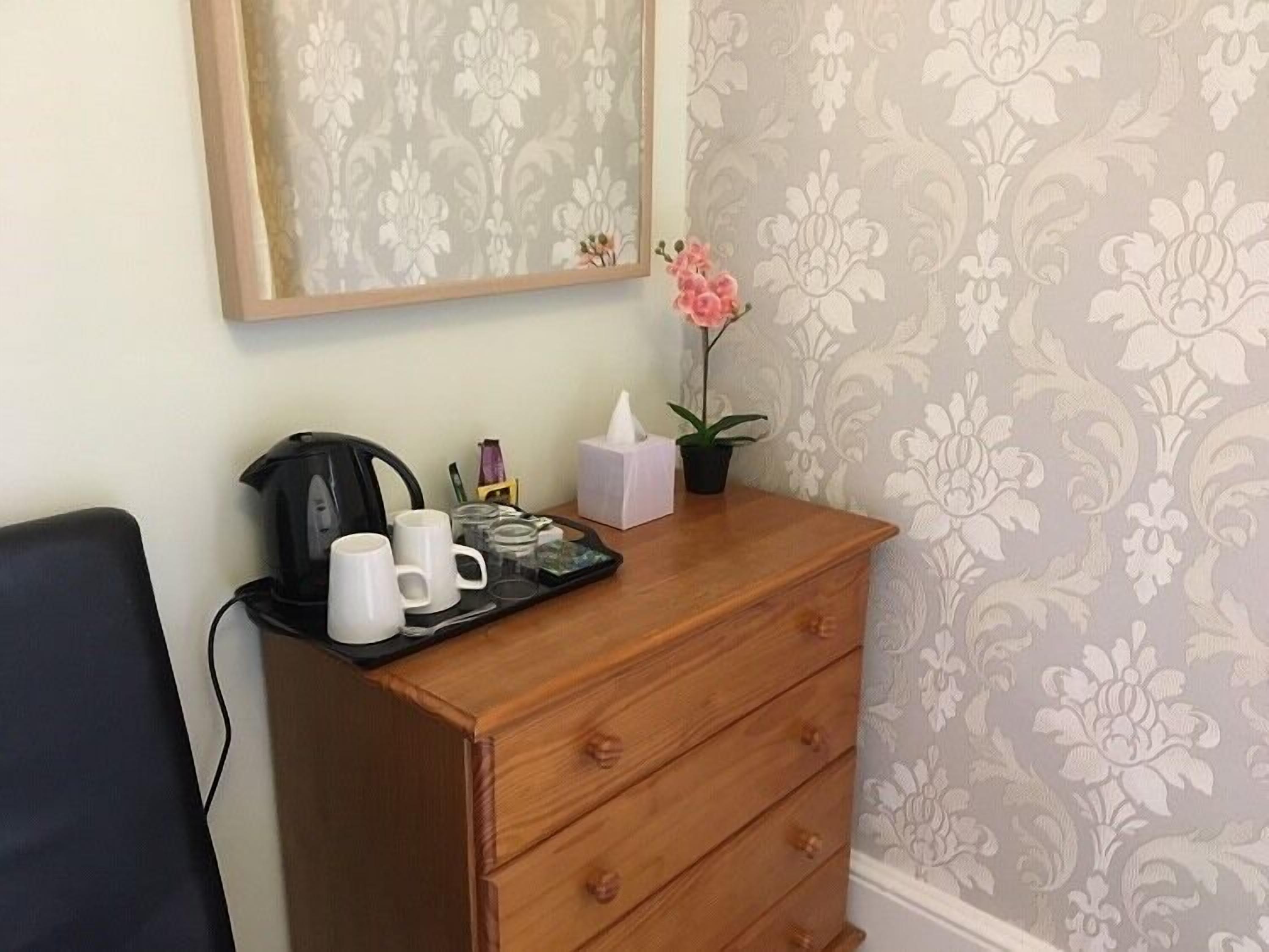 A wooden dresser with a tray of white mugs, a black coffee maker, a tissue box, and a potted pink orchid.