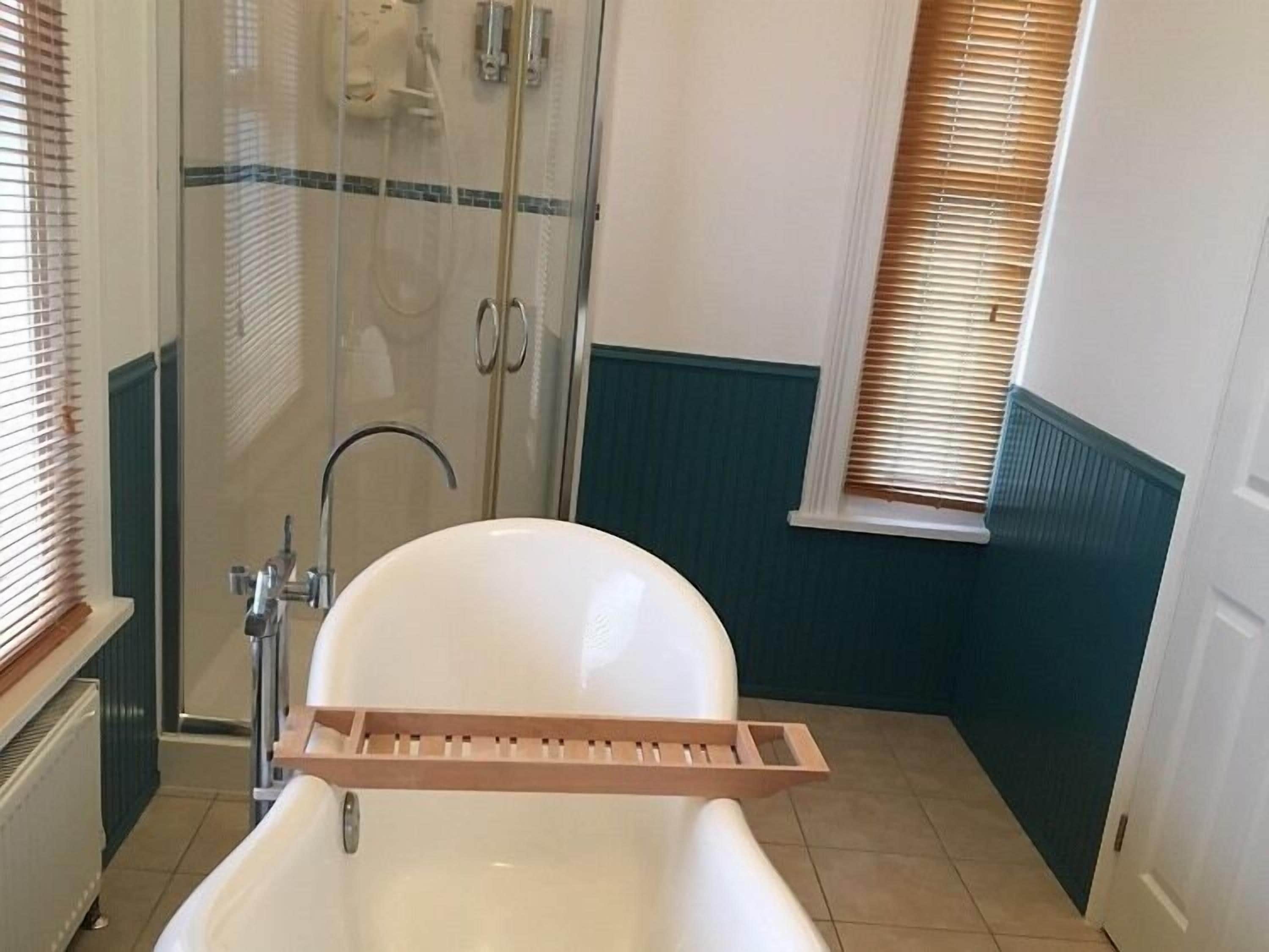 A bathroom with a bathtub, a glass shower enclosure, and a window with blinds.