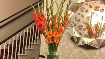Een trap met witte balustrades en een transparante vaas met oranje bloemen tegen een behang met patroon.