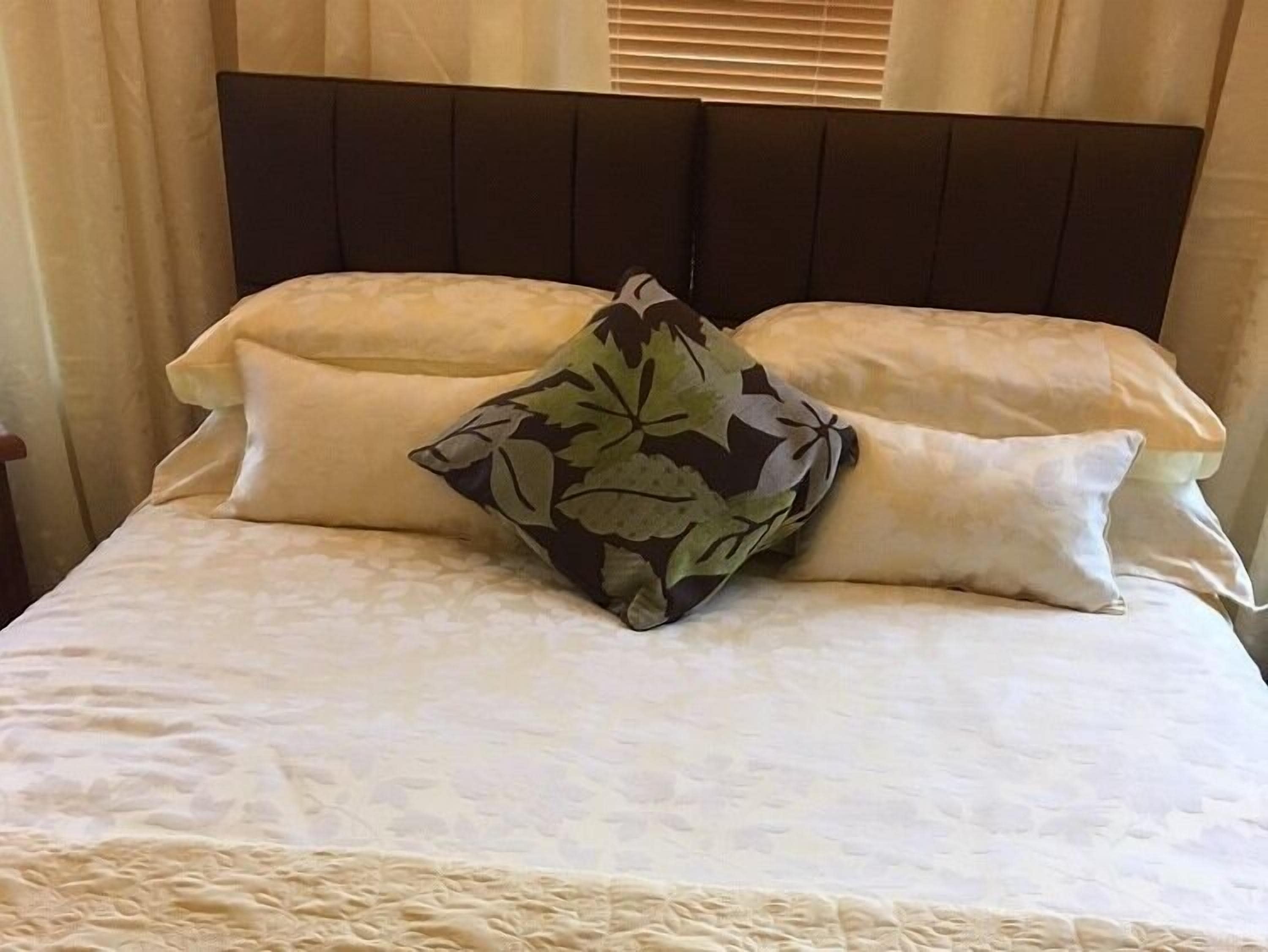 Un lit avec une tête de lit sombre, deux oreillers unis et un oreiller à motifs floraux.