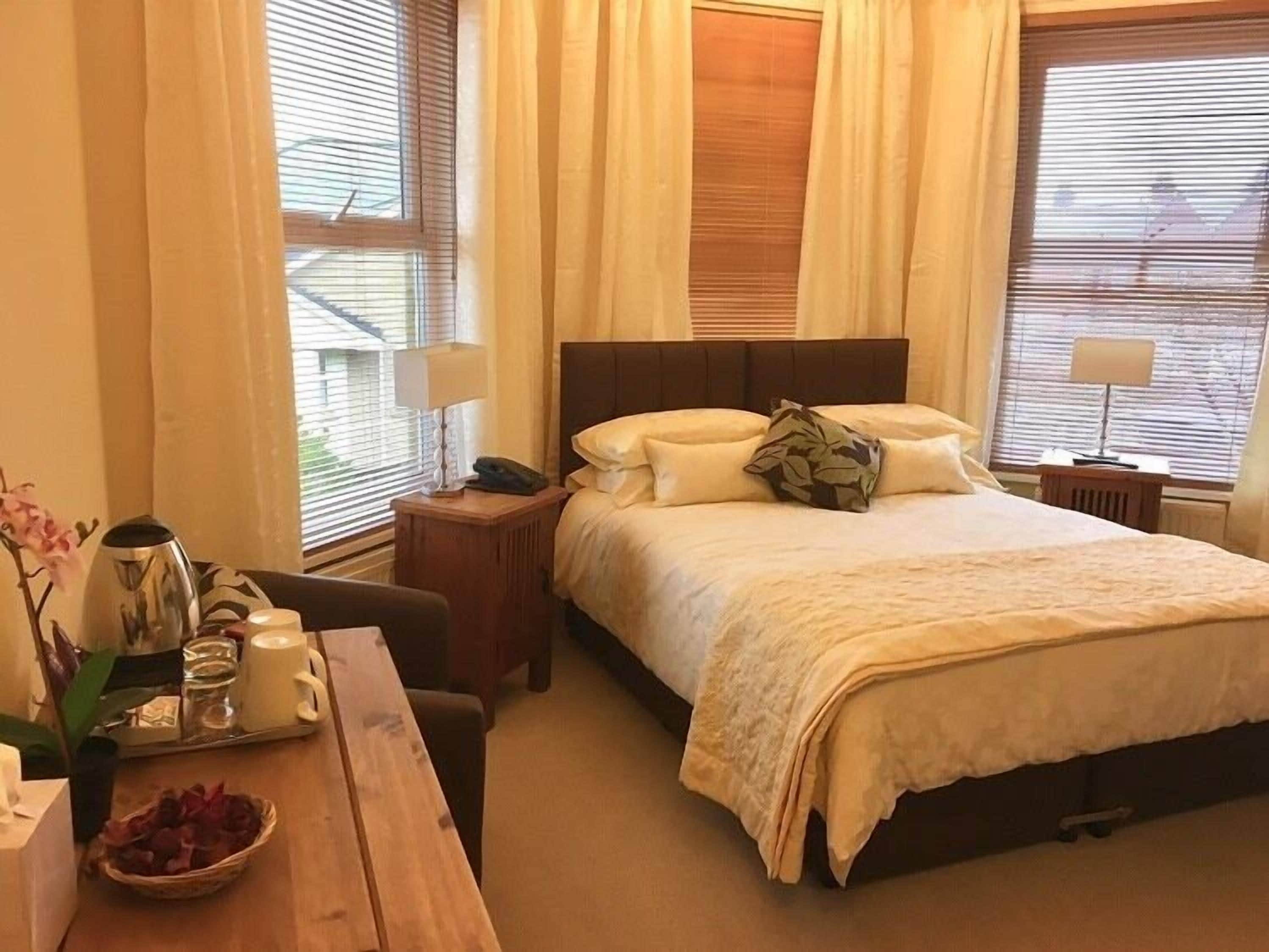 Een hotelkamer met een bed, nachtkastjes, een bureau met lamp en een raam met zonwering.