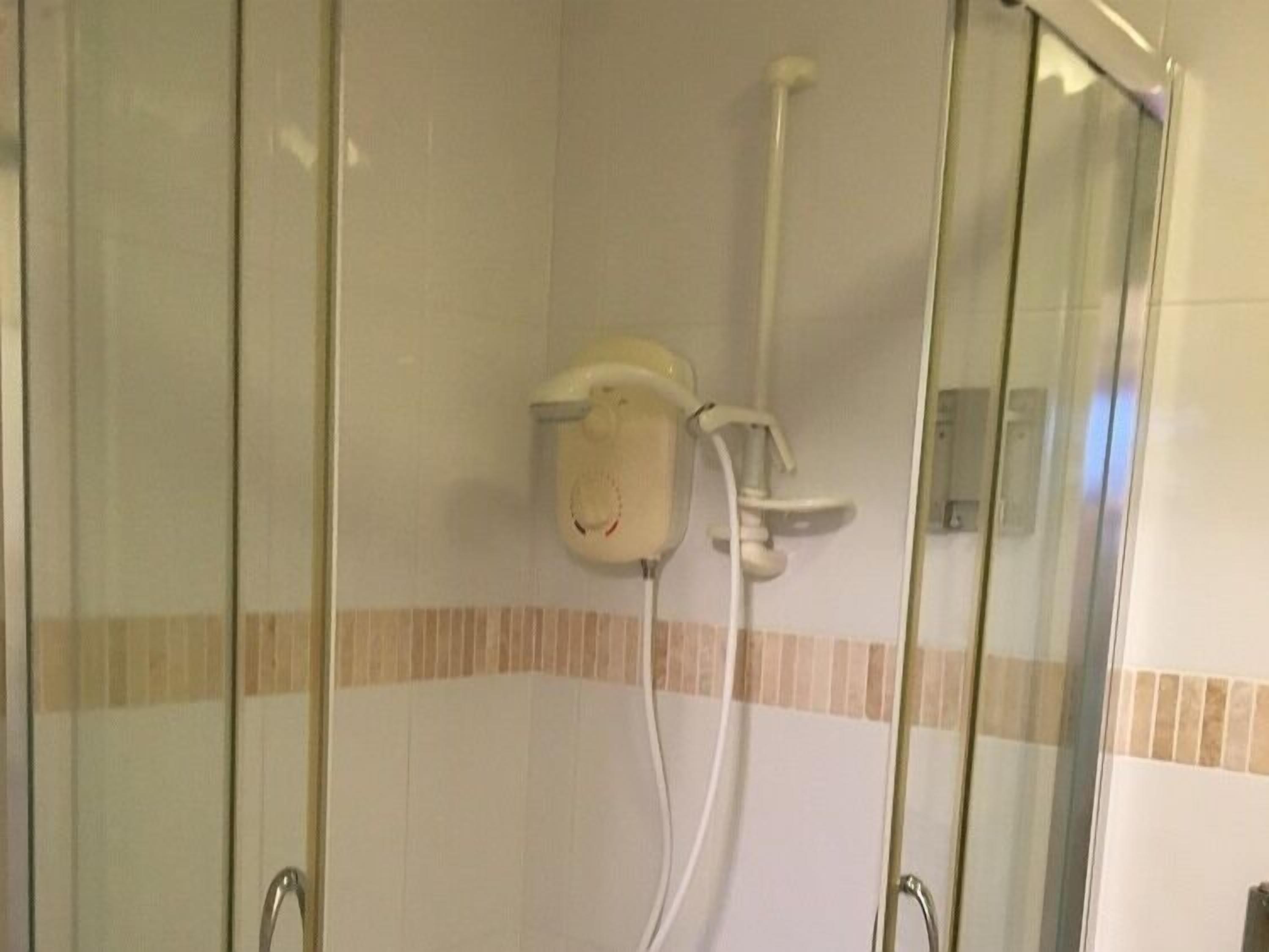 A glass-enclosed shower area with a handheld showerhead and a wall-mounted control panel.