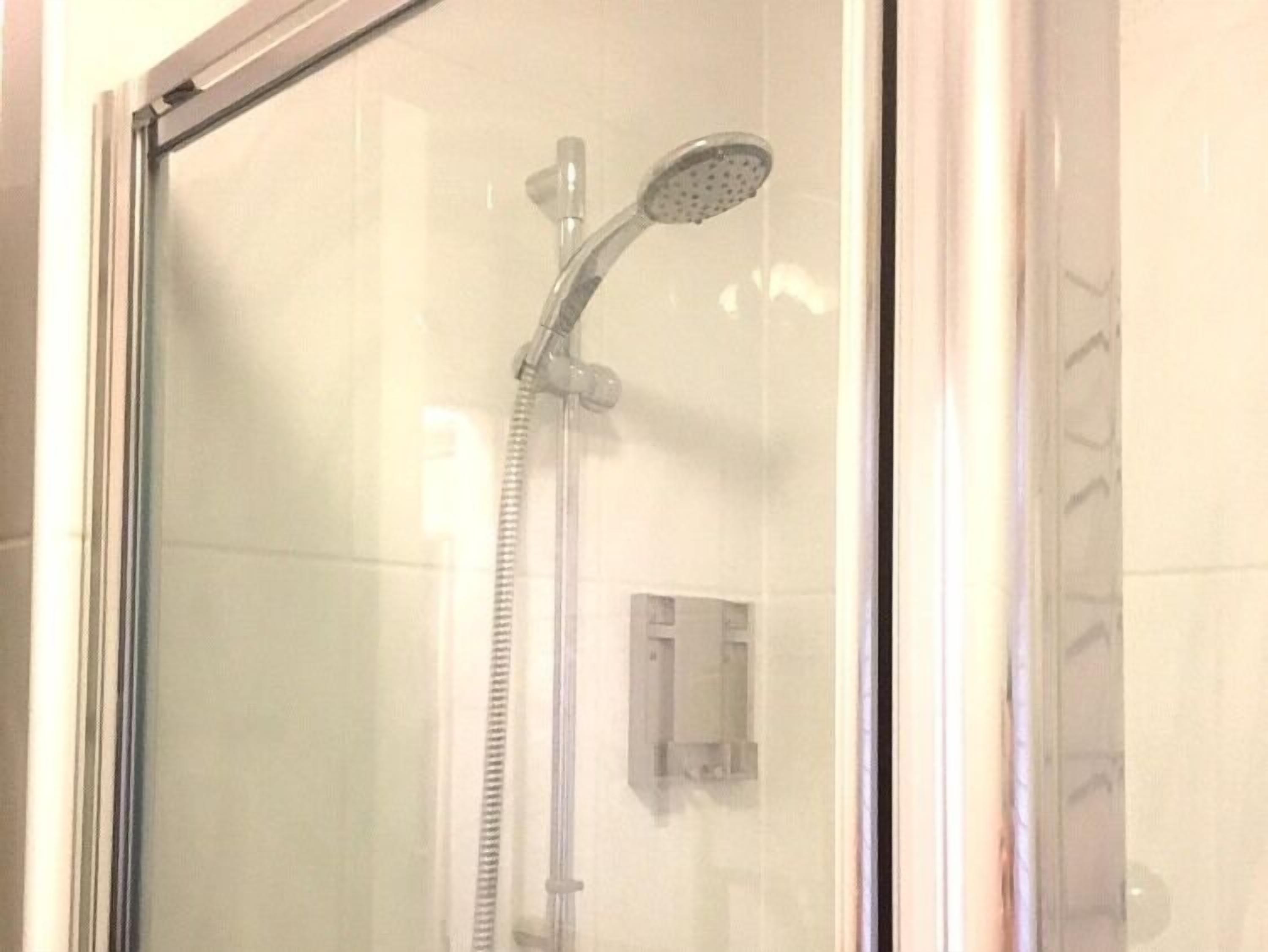 A glass-enclosed shower area with a handheld showerhead and a wall-mounted control panel.