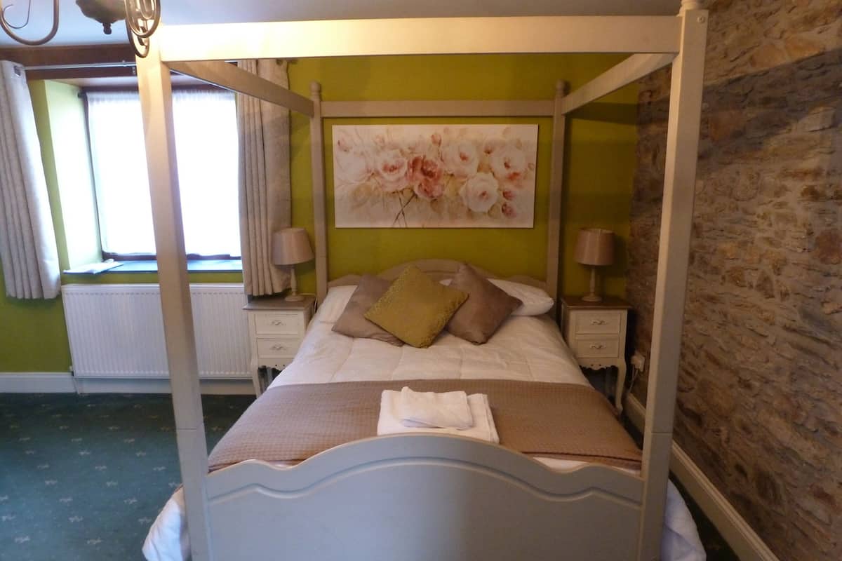 A four-poster bed with a white frame, a green wall with a floral painting, and a stone wall on one side.
