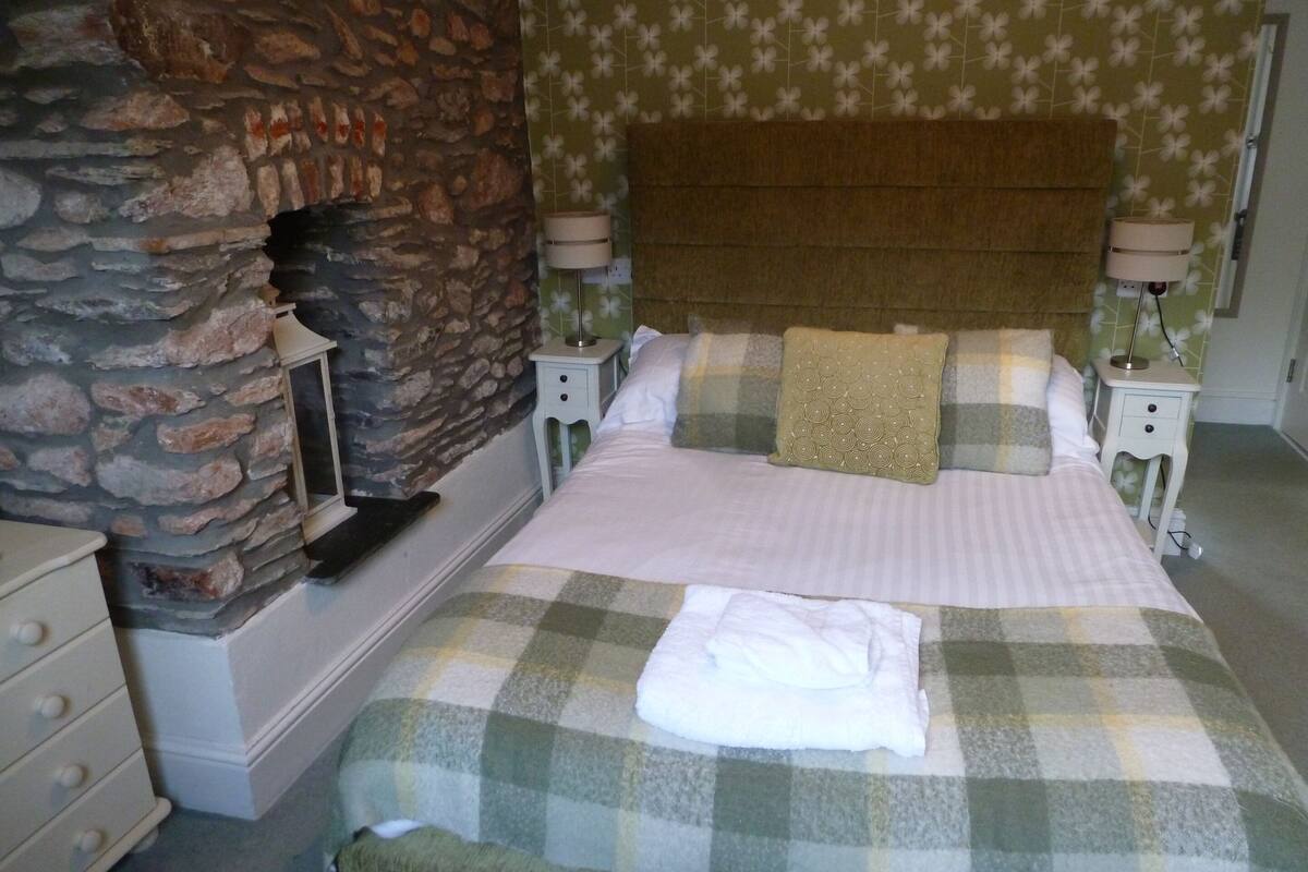 A bedroom with a stone wall, a checkered bedspread, and two bedside tables with lamps.