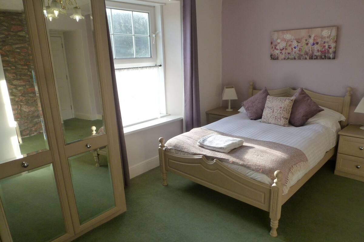 A bedroom with a bed, nightstands, a mirror, and a window.