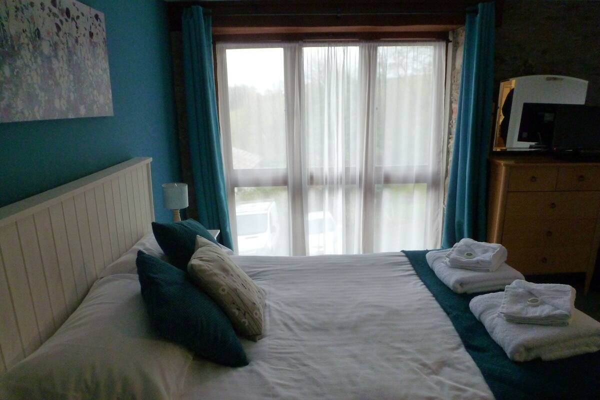 A hotel room with a bed, a dresser, a lamp, and a view of the outdoors through a window.