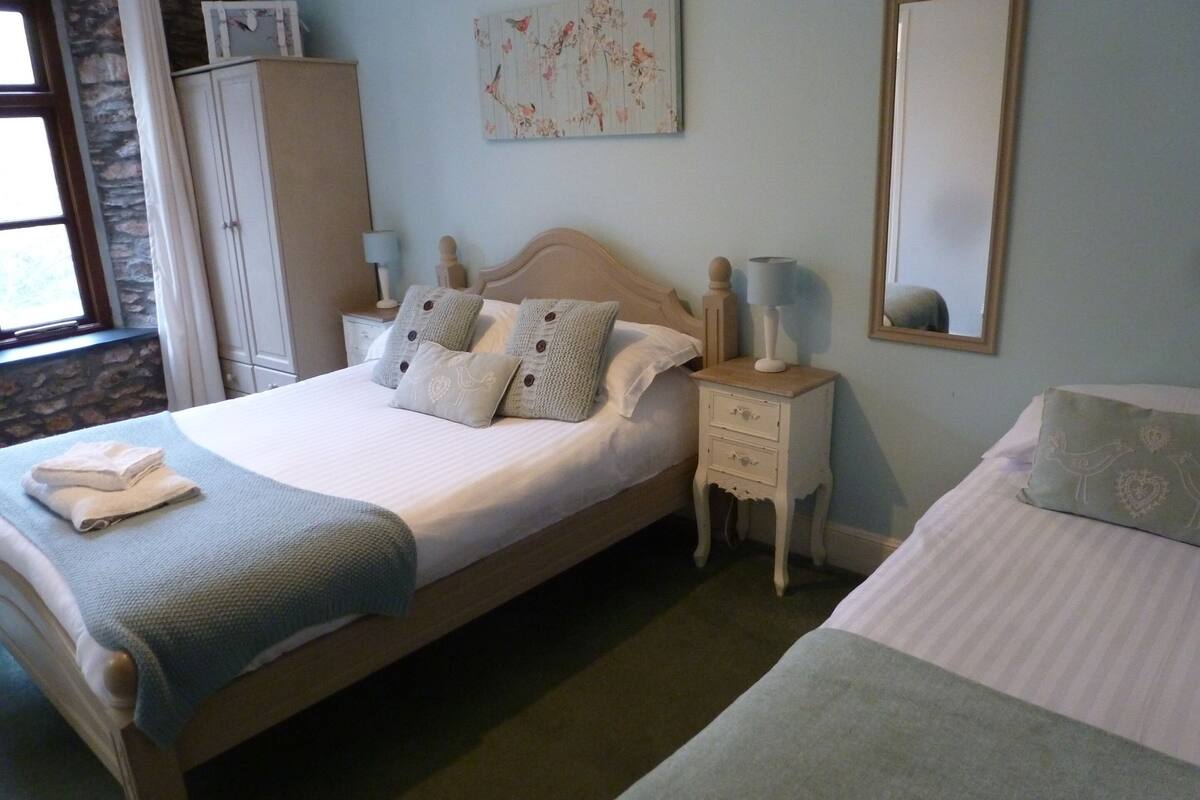 A bedroom with a bed, a nightstand, a dresser, a mirror, and a window.