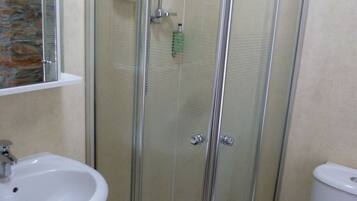 A glass-enclosed shower with a handheld showerhead, a white sink, and a toilet.