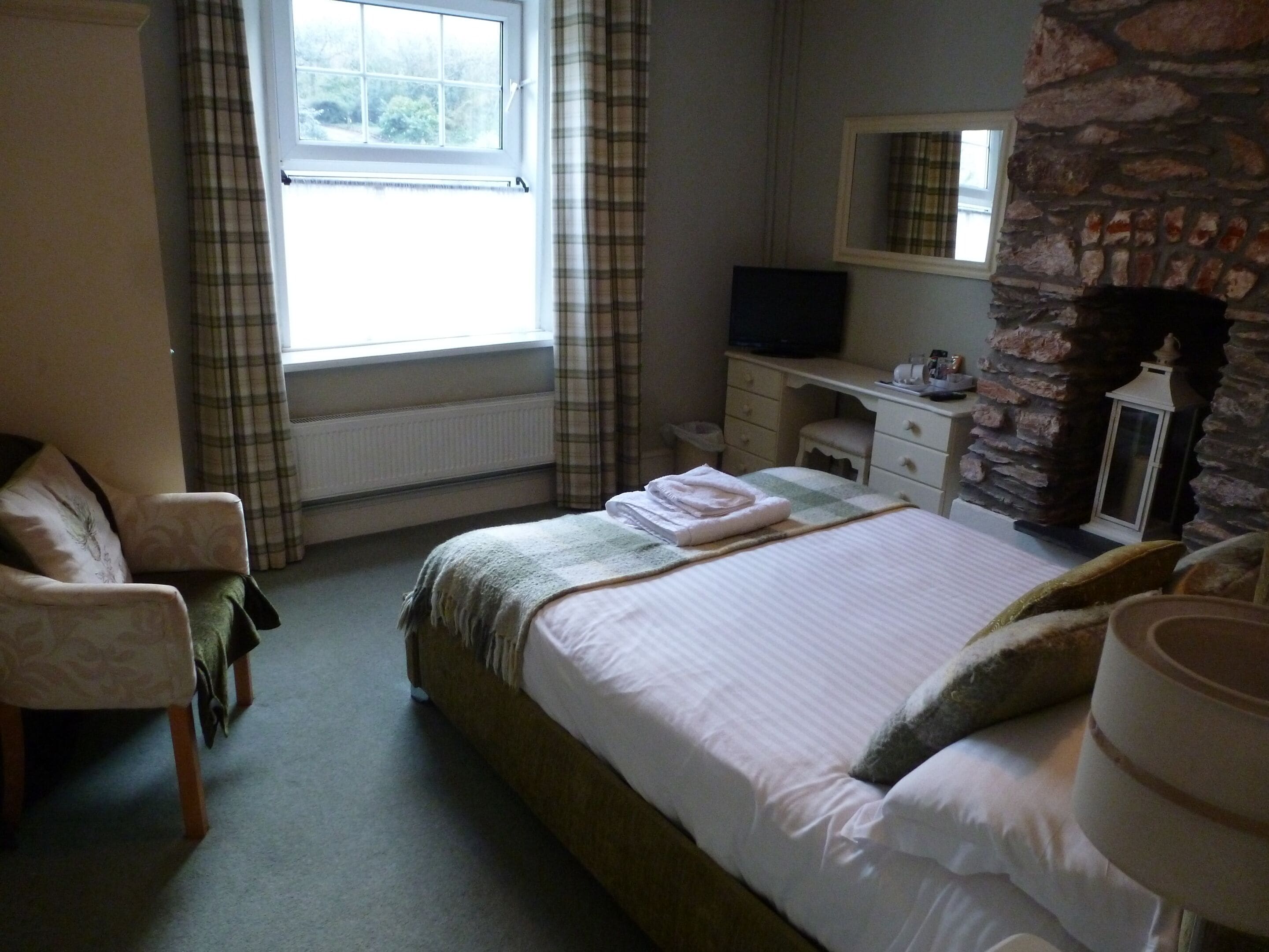 A bedroom with a bed, a chair, a dresser, a television, and a stone wall.