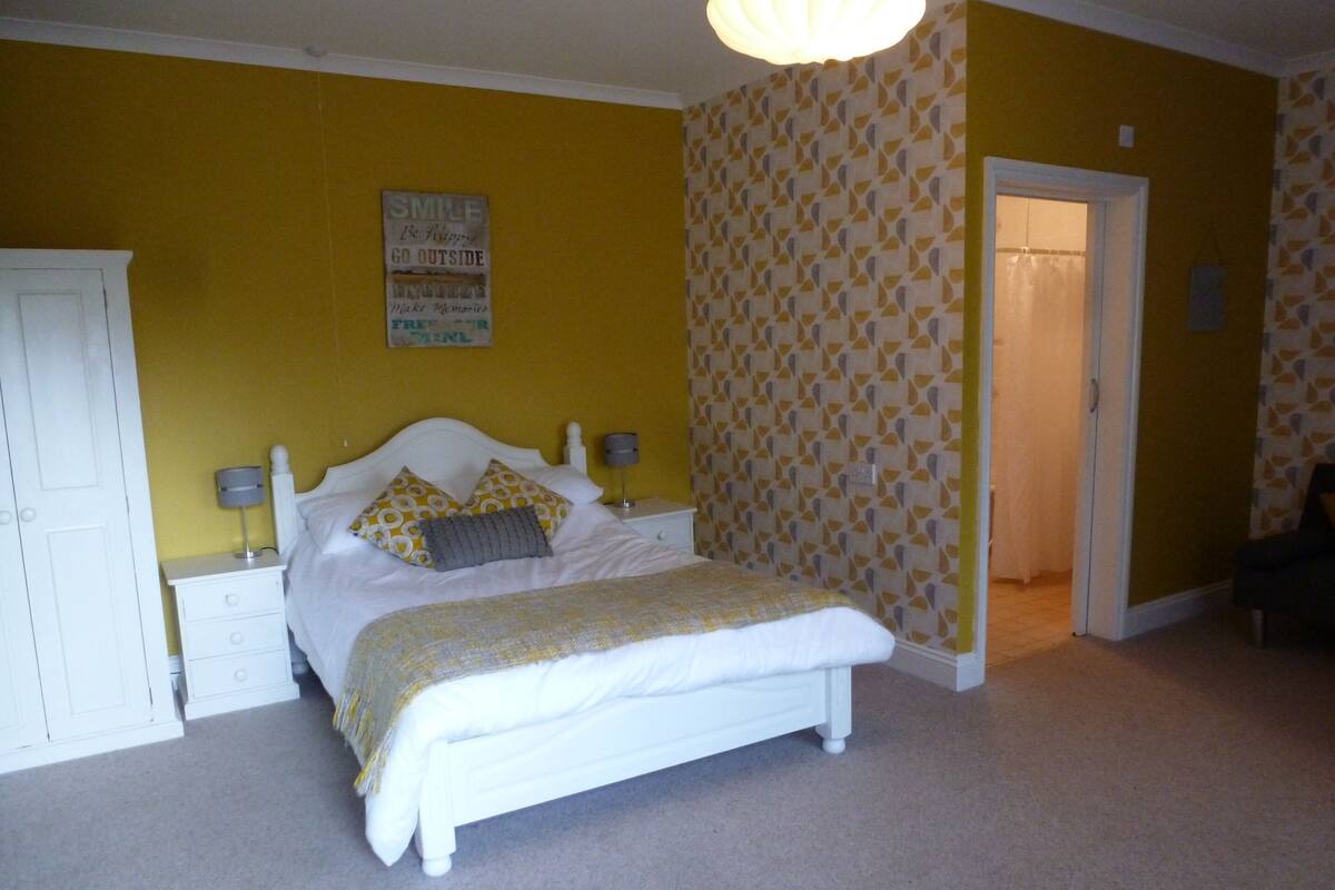 A bedroom with a bed, nightstands, a wardrobe, and a door leading to another room.