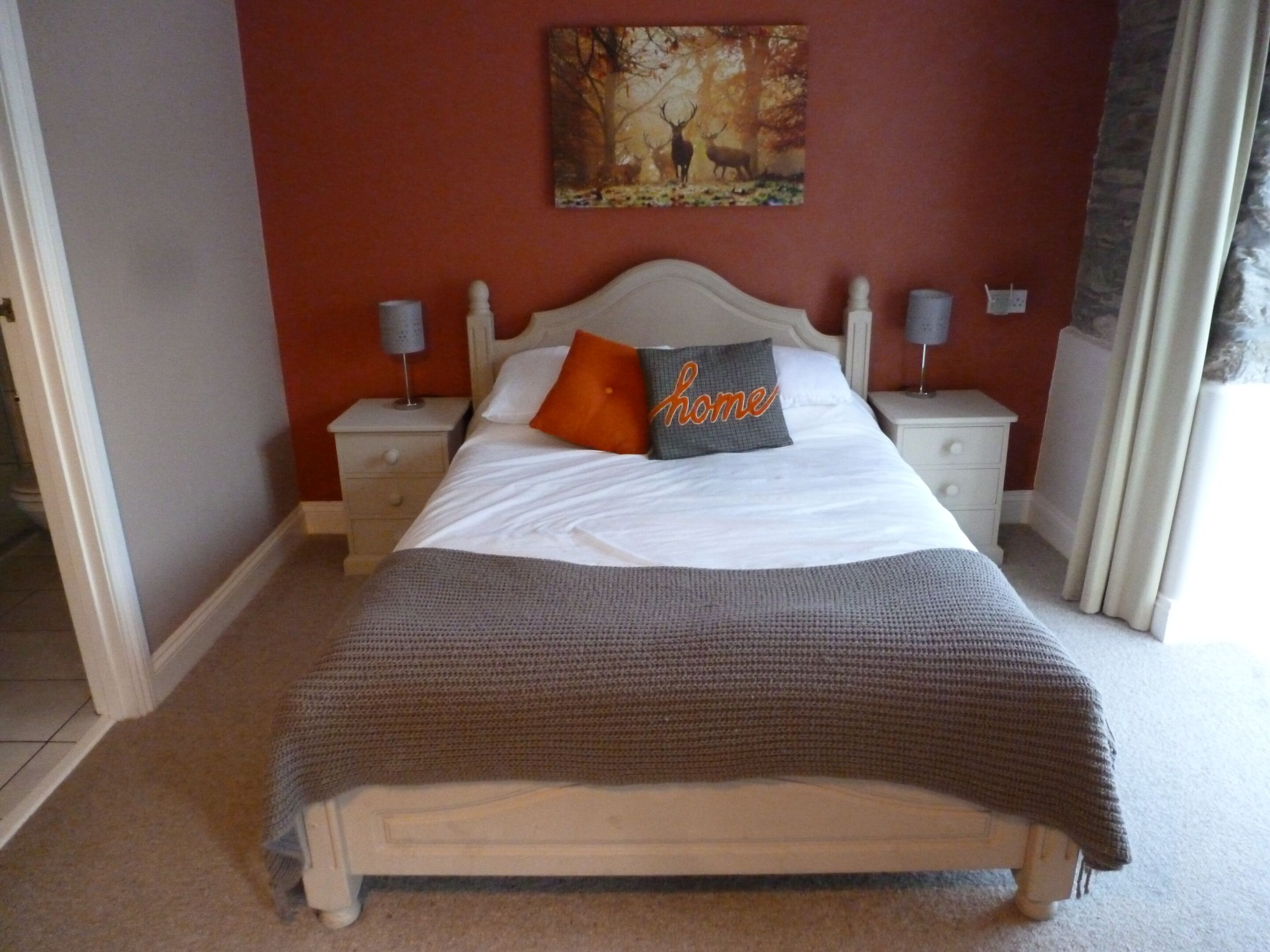 Une chambre à coucher comprenant un lit, deux tables de chevet, une commode, un tableau accroché au mur et une fenêtre avec des rideaux.