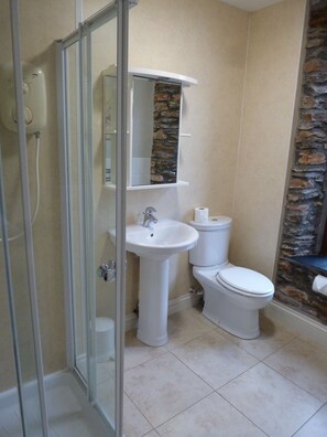 A bathroom with a glass shower enclosure, a pedestal sink, a toilet, and a stone accent wall.