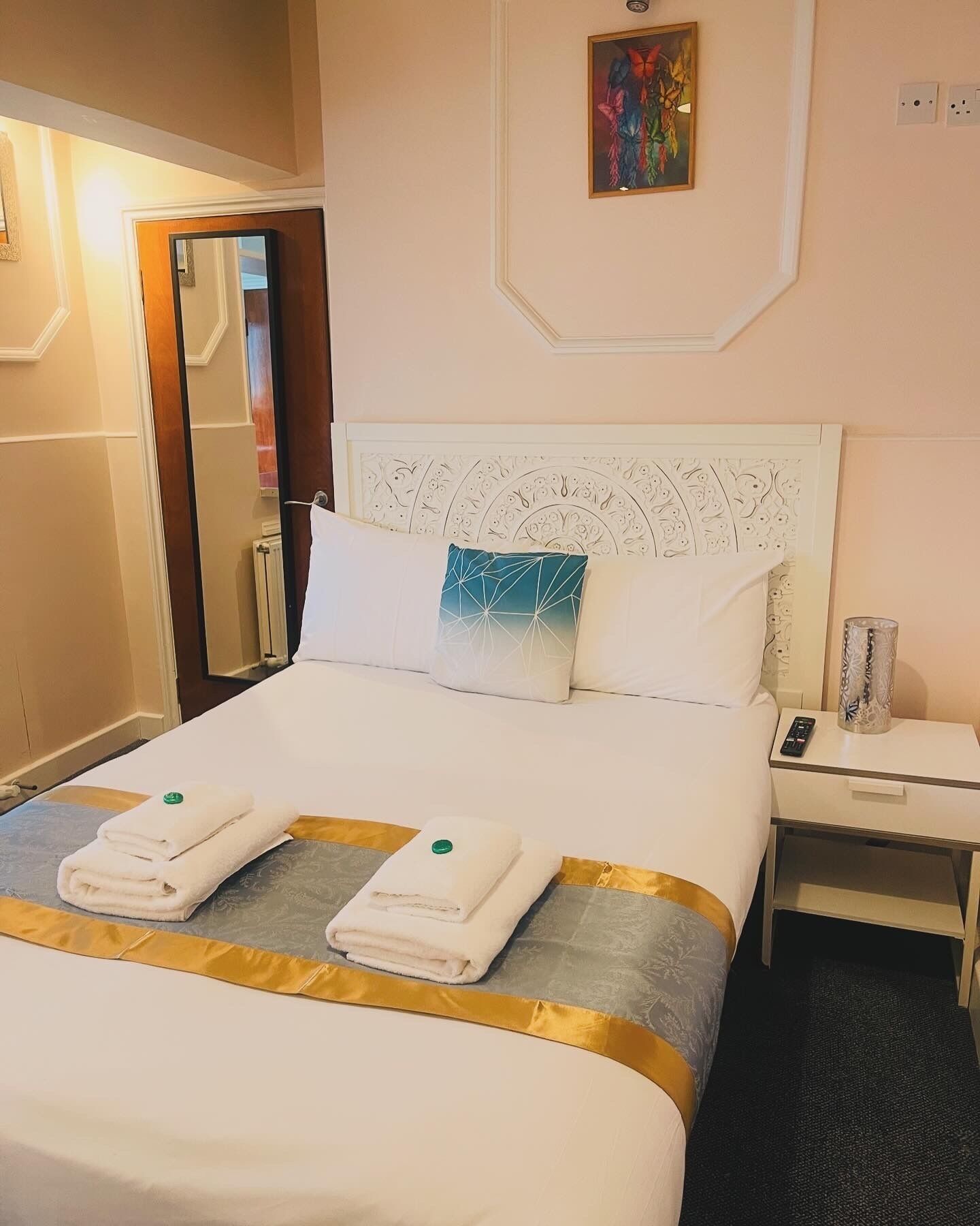 A hotel room with a neatly made bed, a bedside table with a lamp, and a painting on the wall.