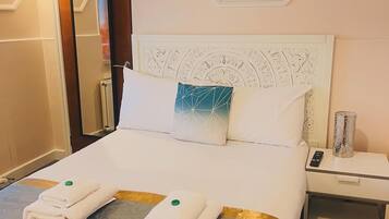 A hotel room with a neatly made bed, a bedside table with a lamp, and a painting on the wall.
