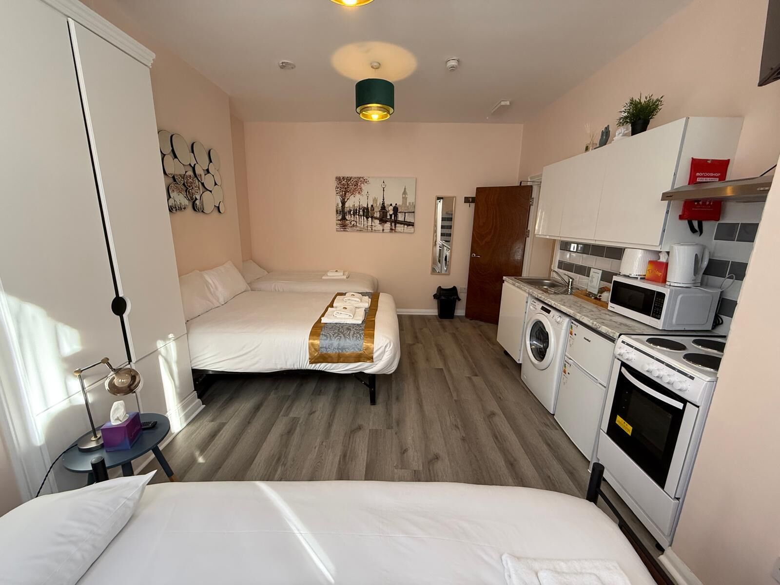 A compact hotel room with two beds, a washing machine, a microwave, and a stove.