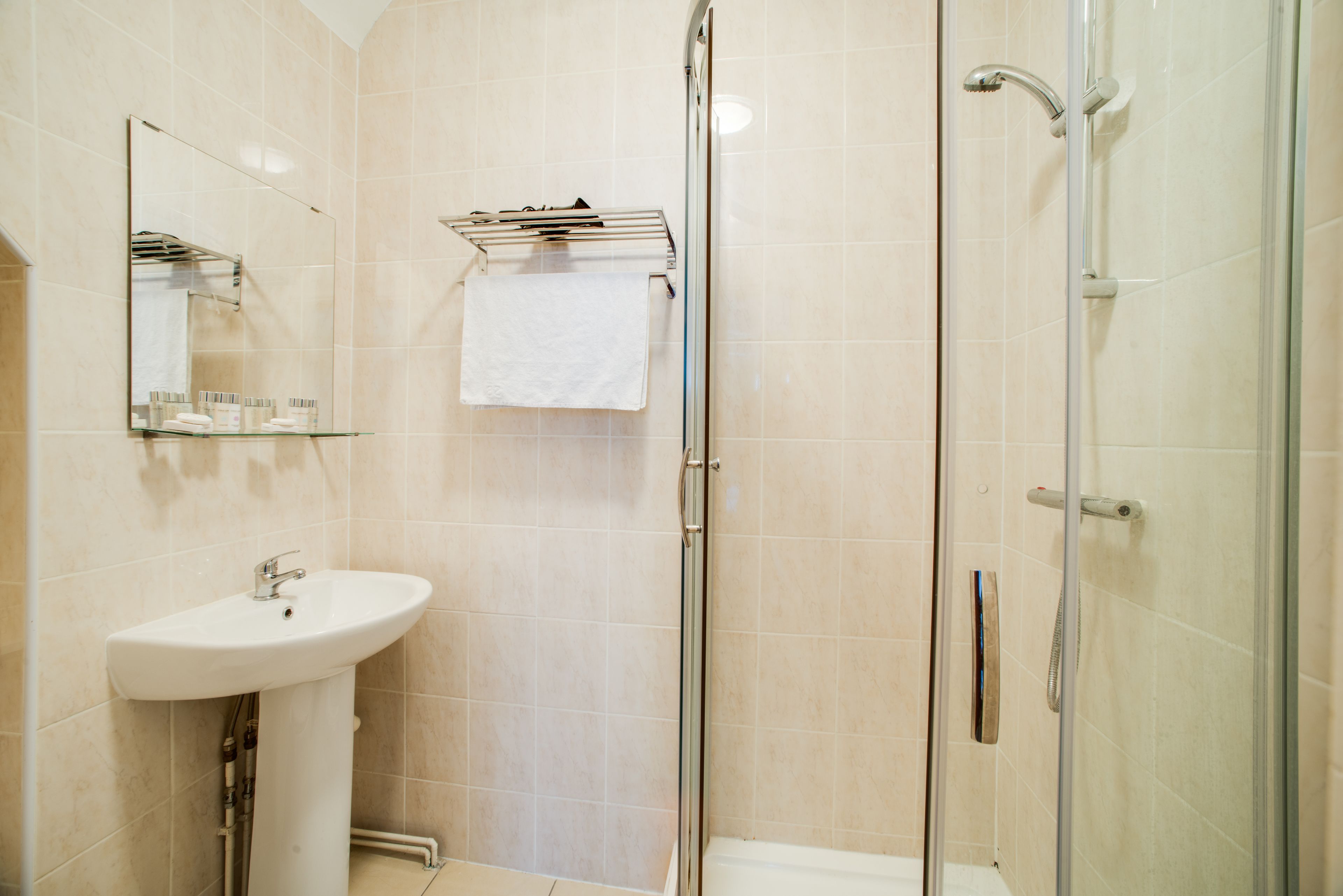 Ein modernes Badezimmer mit Waschbecken, Spiegel, Handtuchhalter und Duschkabine aus Glas.