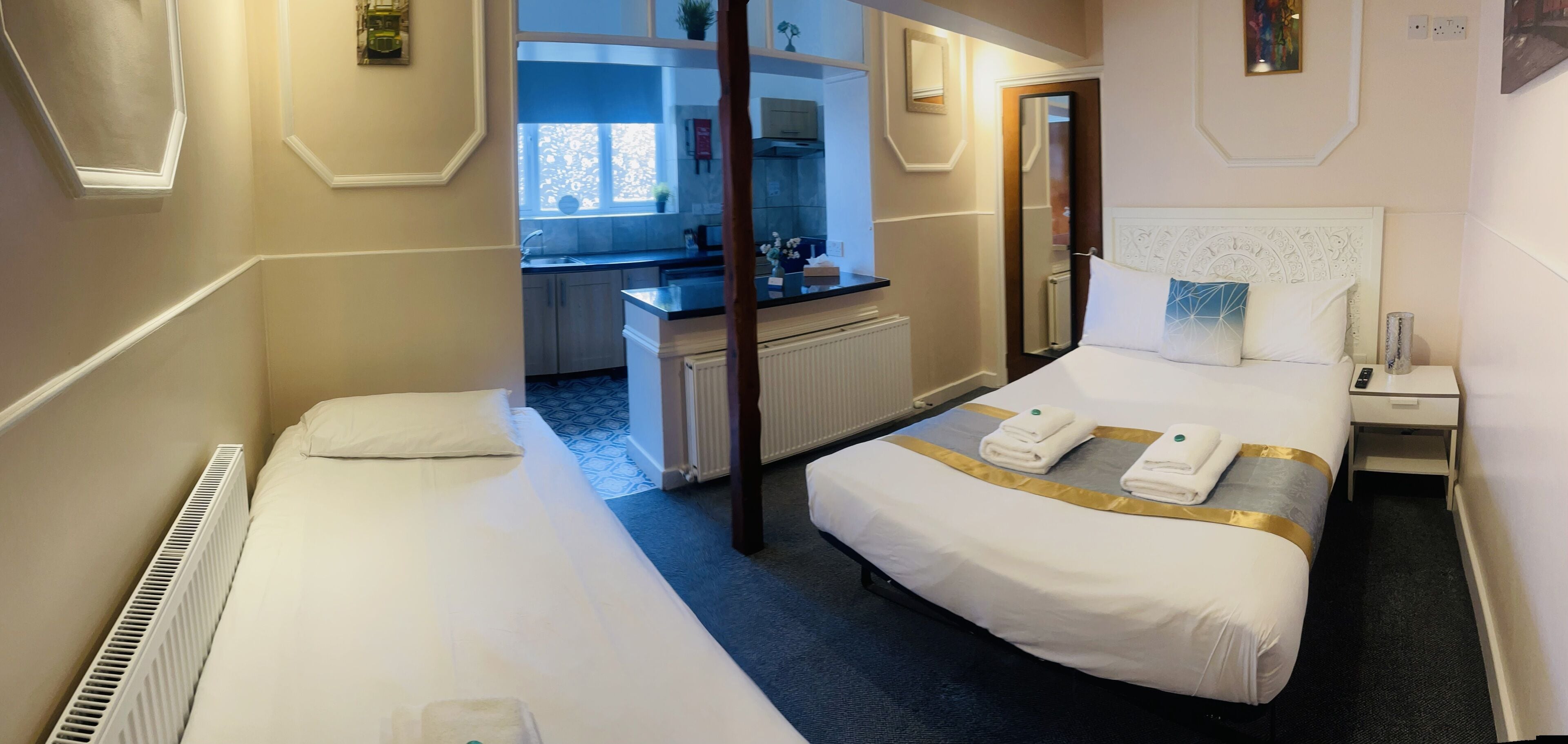 A hotel room with a large bed, a smaller bed, a desk, and a view of the kitchen.