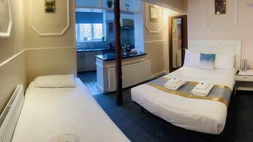 A hotel room with a large bed, a smaller bed, a desk, and a view of the kitchen.